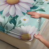 A hand gently touches a fitted mattress protector sheet featuring a white and purple floral print on a teal background.