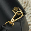 Close-up of a black leather bag featuring gold metal D-shaped ring handles and screws.