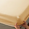 Hands are folding a beige soft touch microfiber fitted sheet with deep pockets.