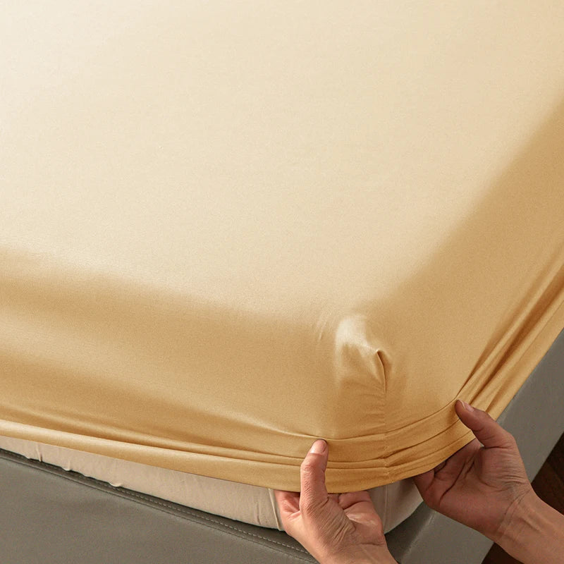 Hands are folding a beige soft touch microfiber fitted sheet with deep pockets.