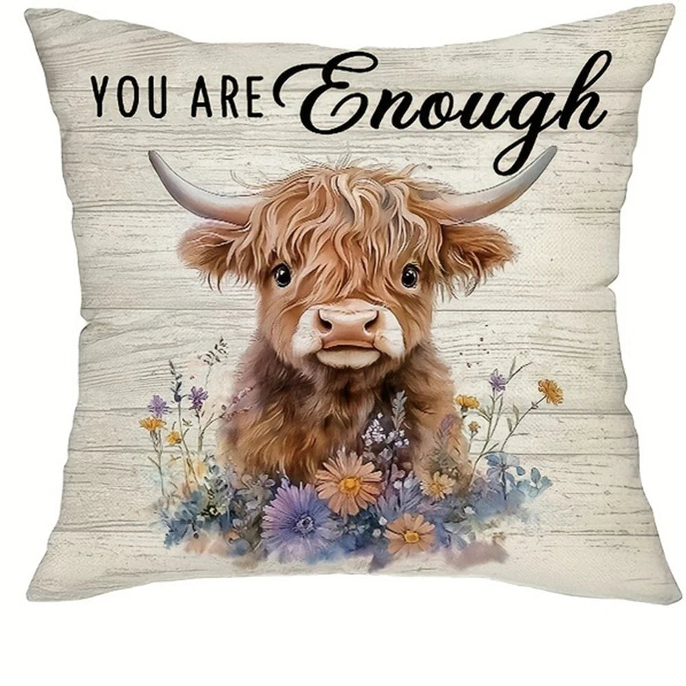 A decorative pillow cover featuring a print of a brown Highland cow with horns surrounded by wildflowers.