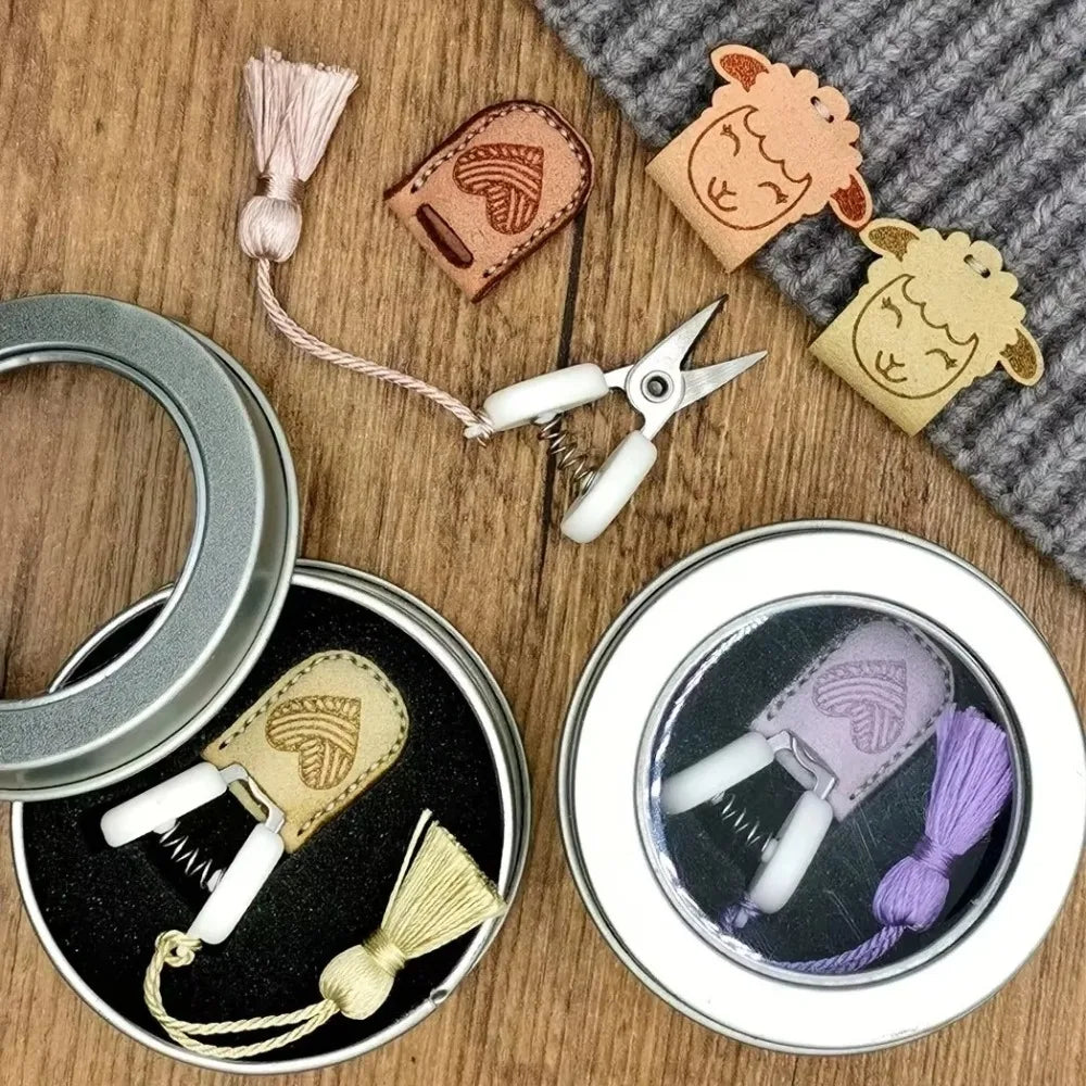 Mini precision sewing scissors with protective leather covers and a purple thread shown on a wooden surface.