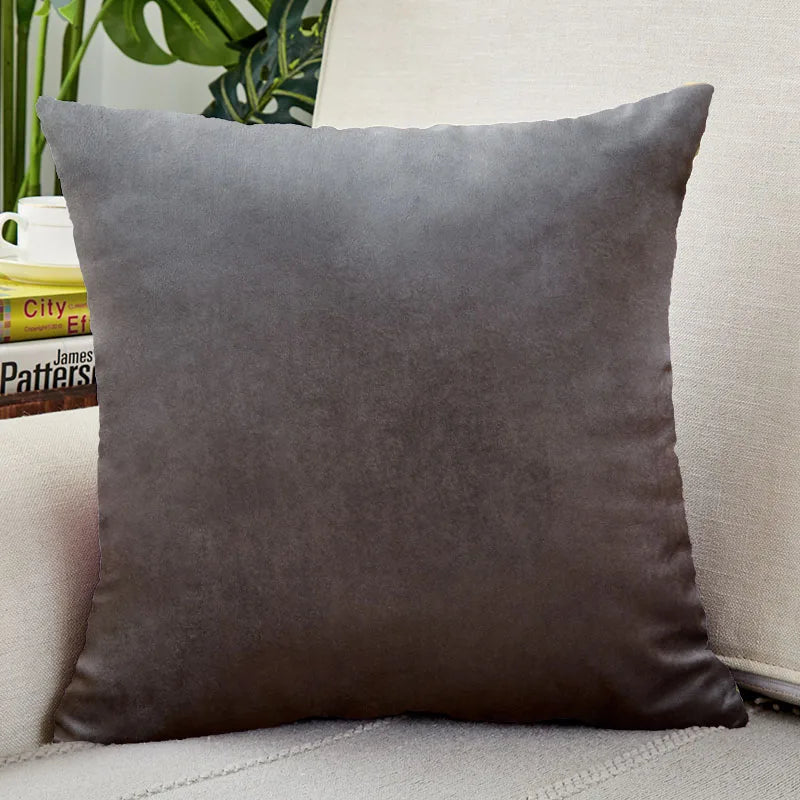 A square, dark gray velvet cushion cover resting on a light-colored sofa.