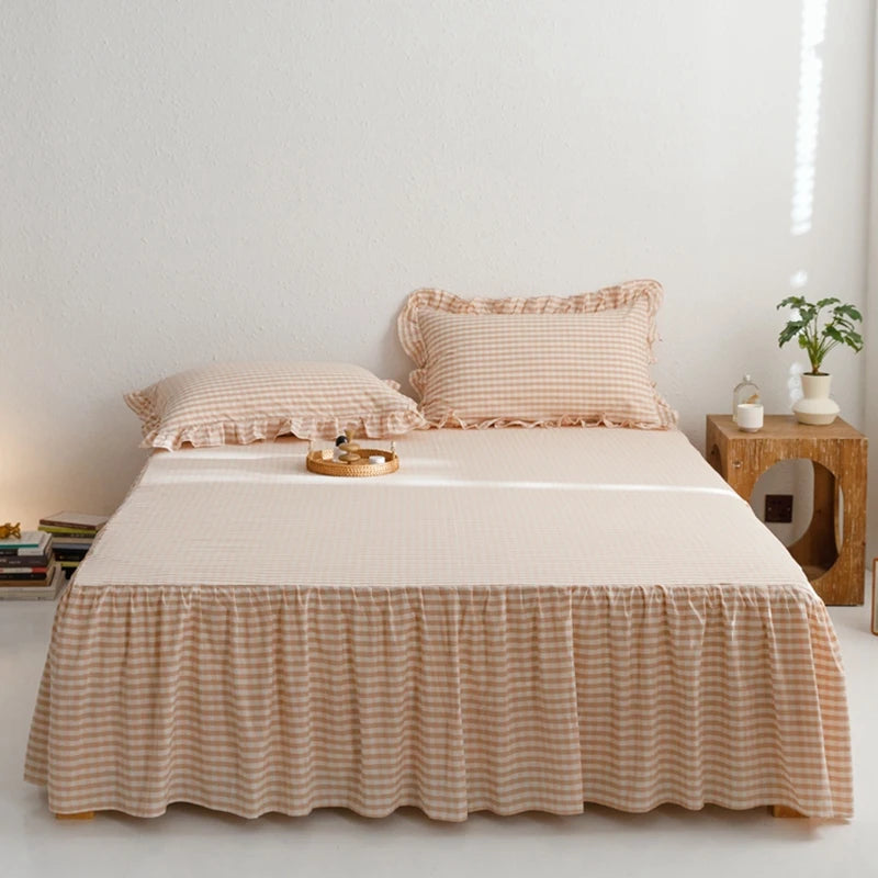 A beige plaid cotton bed skirt cover with a matching pillow and bedding on a light-colored bed.