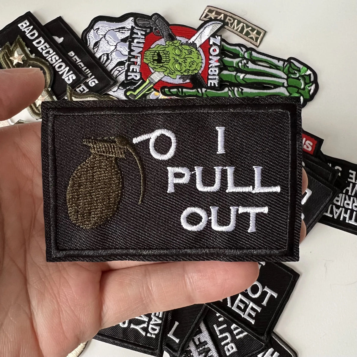 A hand holds several black iron-on slogan patches featuring text and graphics.