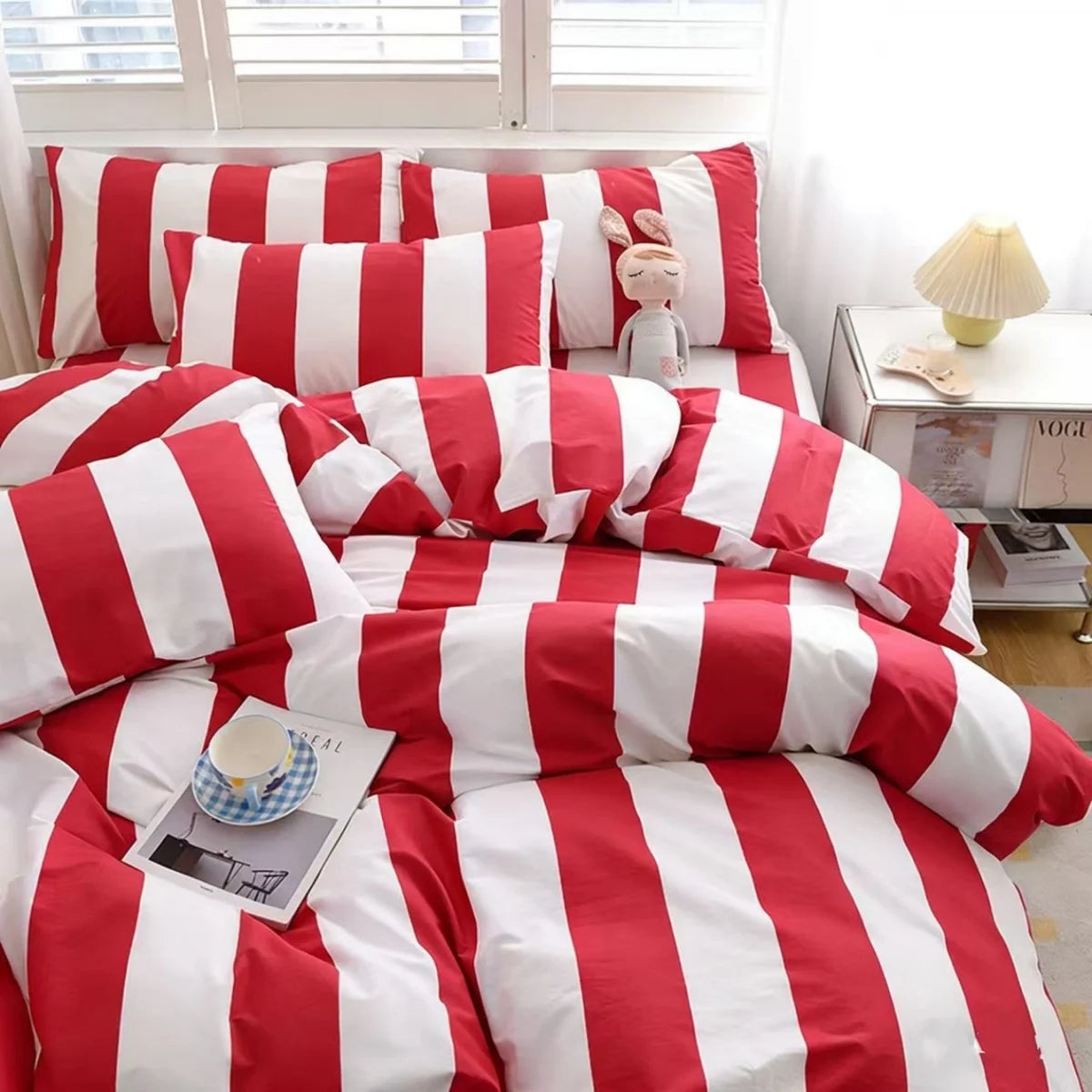 A red and white striped duvet cover set with pillows and a stuffed rabbit toy displayed on a bed.