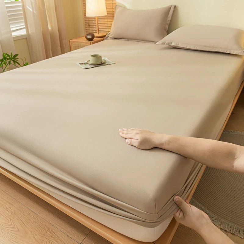 A hand is adjusting a beige fitted sheet on a bed, showing the smooth fabric and bedding.