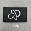 Black embroidered patch with a white stylized symbol on a gray background