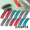 A set of silicone pan handle covers in various colors including pink, blue, and gray, shown next to a metal pot handle.