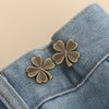 A pair of gold-toned clover-shaped brooches pinned onto a blue denim fabric.