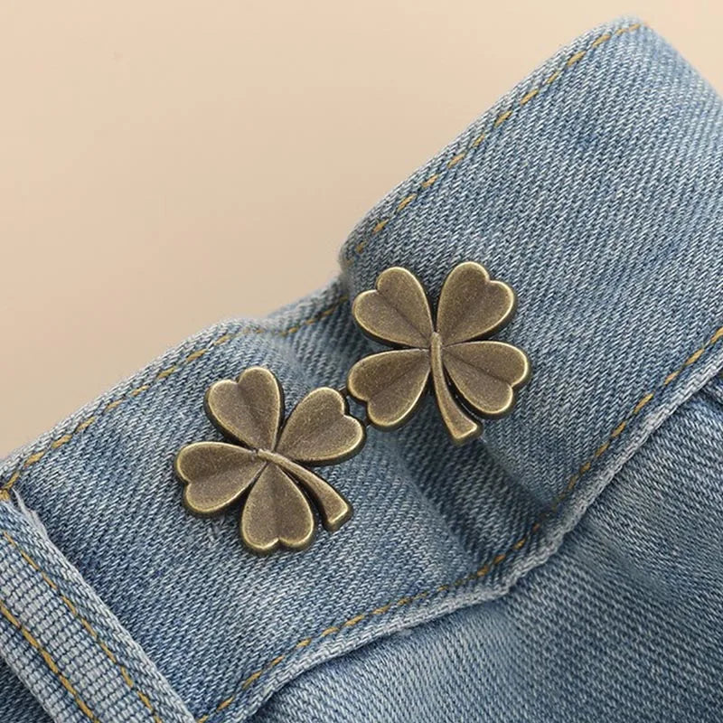 A pair of gold-toned clover-shaped brooches pinned onto a blue denim fabric.