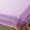 Hands are folding a purple soft touch microfiber fitted sheet with deep pockets.