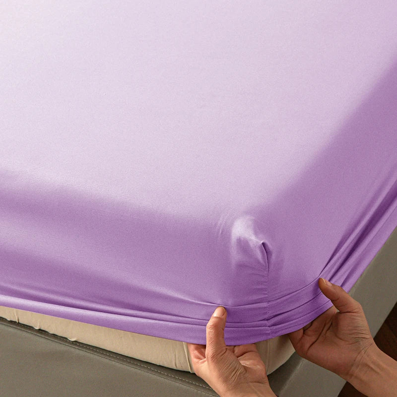 Hands are folding a purple soft touch microfiber fitted sheet with deep pockets.