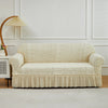 A cream-colored jacquard stretch sofa cover displayed on a light-colored sofa against a white wall.