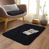 A plush solid black area rug placed on a wooden floor in a living room setting.