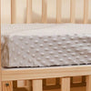 A white soft plush mattress and diaper changing cover placed on a wooden crib rail.