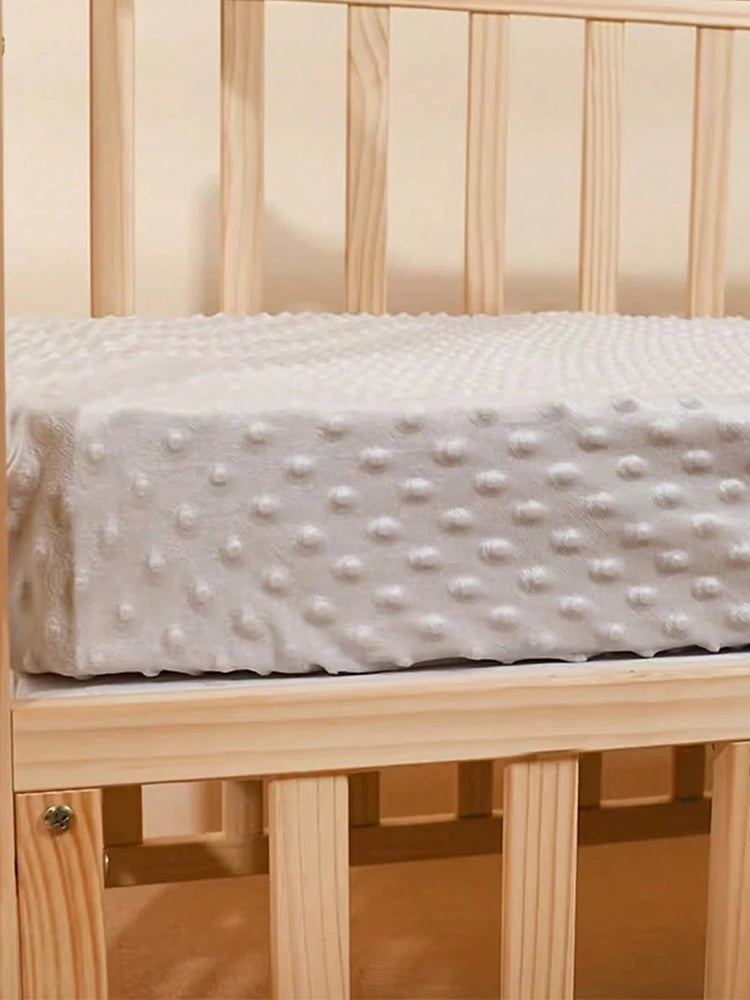A white soft plush mattress and diaper changing cover placed on a wooden crib rail.