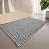 A gray waffle design non-slip bathroom mat placed on a light-colored floor next to a white sofa.
