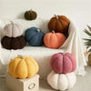 A collection of soft, fuzzy plush pumpkins in various earthy tones like orange, brown, and gray displayed on a white surface.