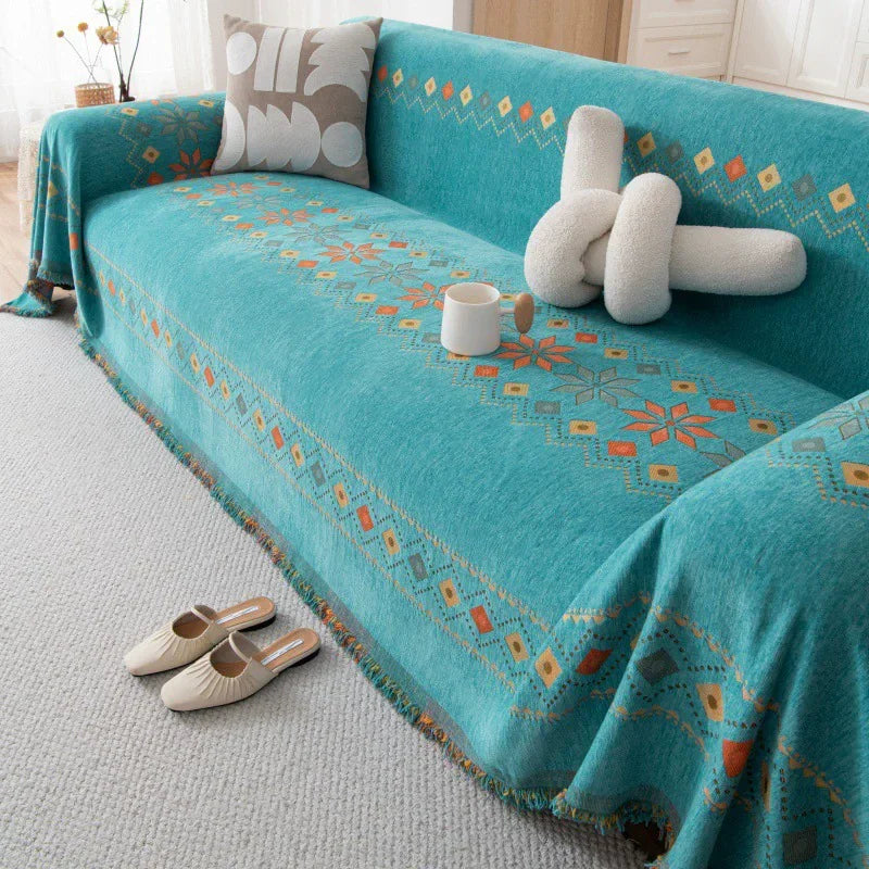 A teal bohemian accent sofa cover draped over a light gray sofa, featuring geometric patterns and cream pillows.
