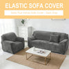 A dark gray elastic sofa cover is displayed on a velvet sofa in a bright living room setting.