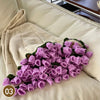 A hand knitted floral rose bouquet throw blanket in purple and green textures resting on a light colored sofa.