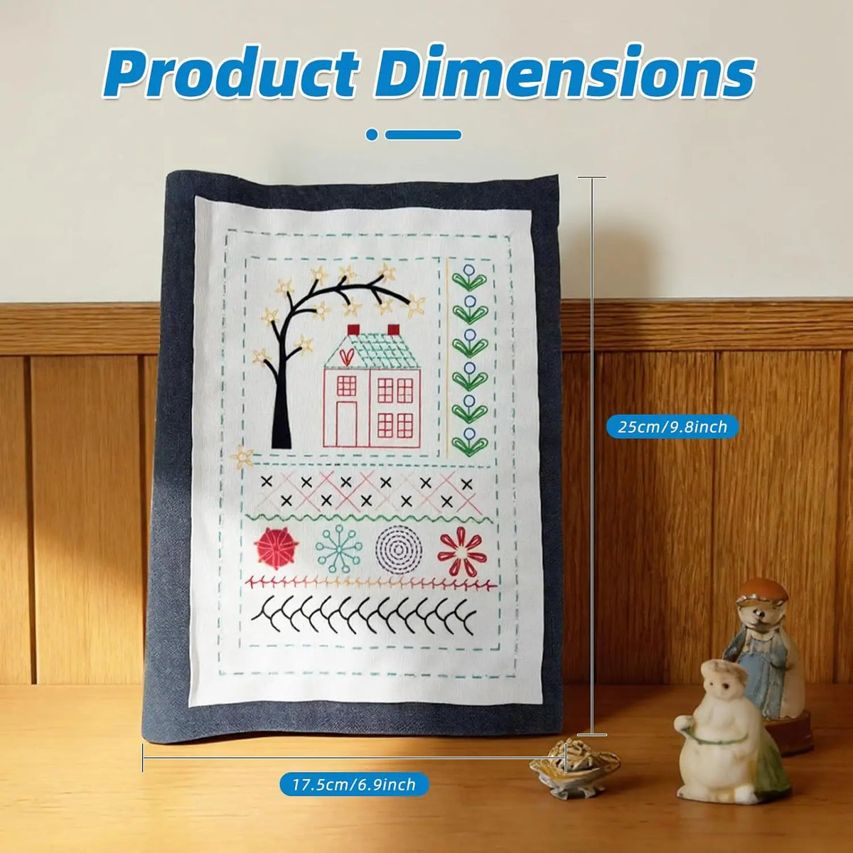 A dark gray fabric featuring a hand embroidery design of a tree, house, and various floral and winter motifs.