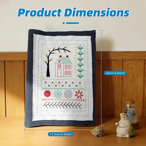 A dark gray fabric featuring a hand embroidery design of a tree, house, and various floral and winter motifs.