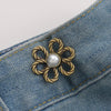 A gold-toned metal waist clip with a pearl center is attached to a blue denim fabric.