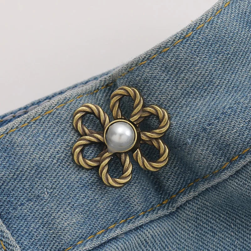 A gold-toned metal waist clip with a pearl center is attached to a blue denim fabric.