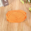 A ball of bright orange flat thread yarn is displayed on a wooden surface.
