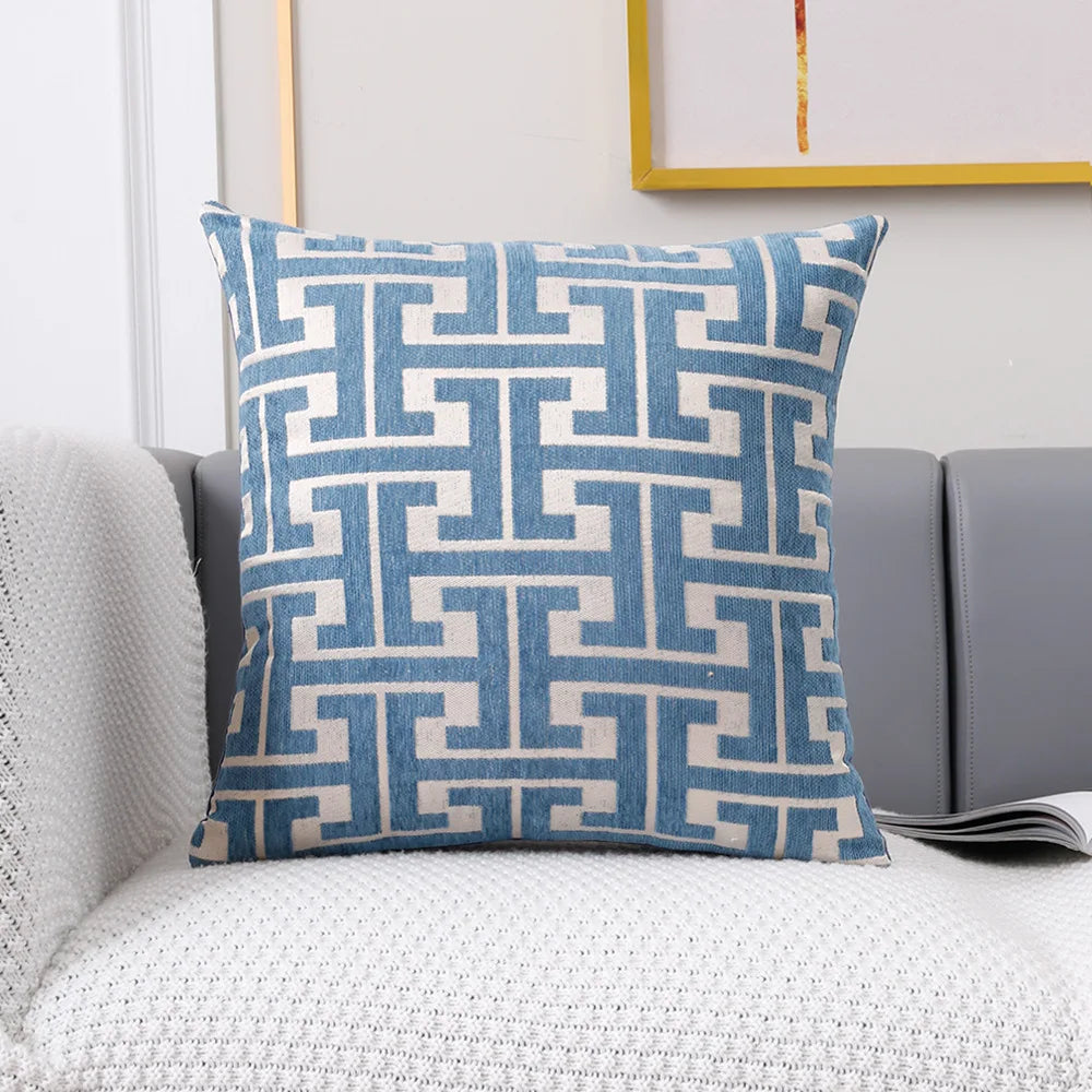 A blue and beige geometric patterned lumbar pillow cover resting on a gray sofa.