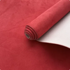 A roll of reddish-orange suede fabric with a white backing is shown on a red surface.