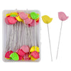 A clear plastic box containing dressmaking pins with colorful heads in pink, yellow, and green.