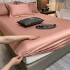 A close-up of a pink fitted bed sheet with decorative pillows and accessories on a bed.