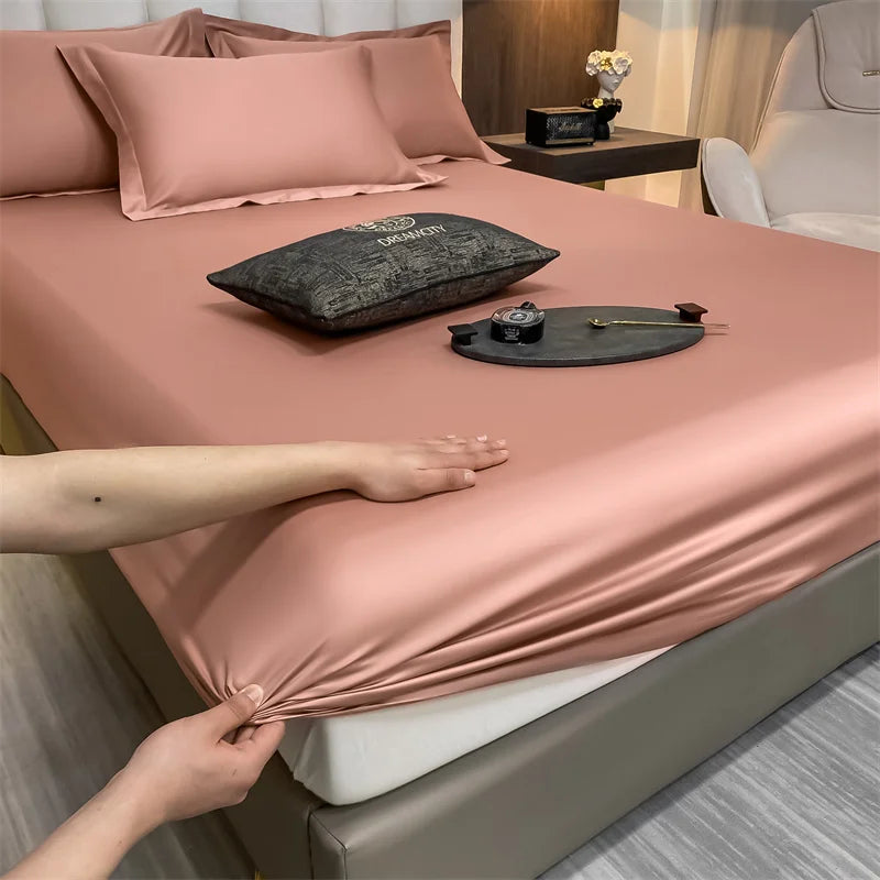 A close-up of a pink fitted bed sheet with decorative pillows and accessories on a bed.