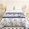 A white floral summer duvet with blue accents displayed on a bed in a bright room.