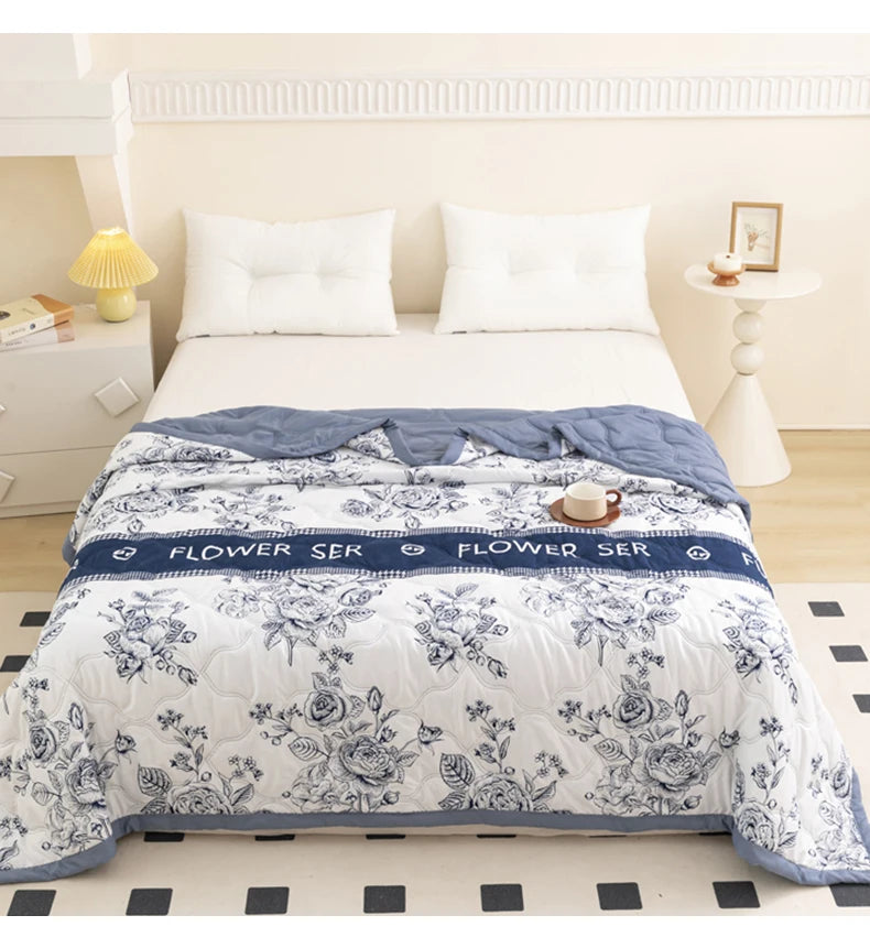 A white floral summer duvet with blue accents displayed on a bed in a bright room.