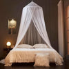A sheer white dome mosquito net draped over a bed, creating a canopy effect in a dimly lit room.