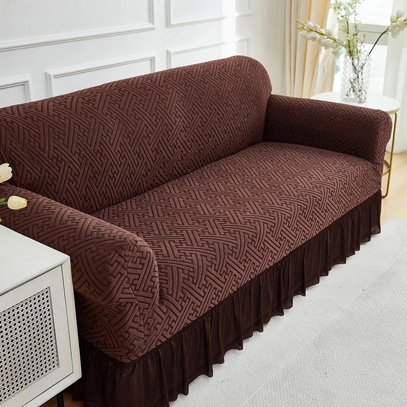 A dark brown jacquard stretch sofa cover draped over a sofa in a bright room.