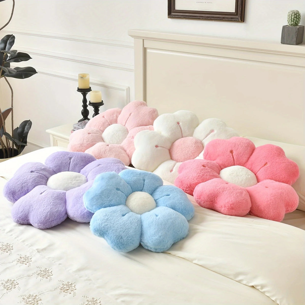 A collection of plush daisy flower throw pillows in shades of pink, purple, and blue arranged on a white bed.