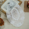 A white oval lace doily or coaster with intricate floral embroidery displayed on a light surface.
