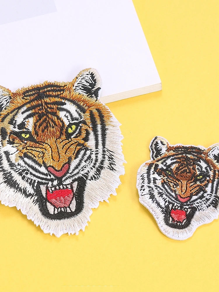 A detailed embroidery patch featuring a tiger's face in black, white, and orange tones on a yellow background.