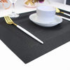 A set of six black non-slip heat resistant placemats is displayed on a white table with silverware and a white cup.