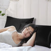 A woman rests her head on a black satin pillowcase in a bright bedroom setting.