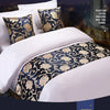 A close-up of a luxurious bed featuring white linens and decorative gold patterned bed tails on the pillows.