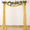 A golden sequin table runner draped across a wooden archway decorated with greenery and flowers.