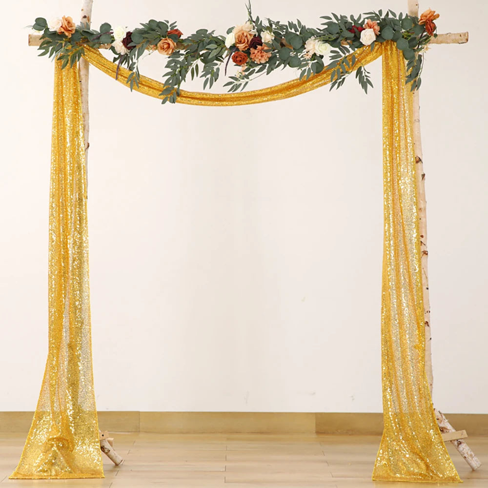 A golden sequin table runner draped across a wooden archway decorated with greenery and flowers.