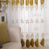 White sheer gauze curtain with gold embroidery hanging in a window