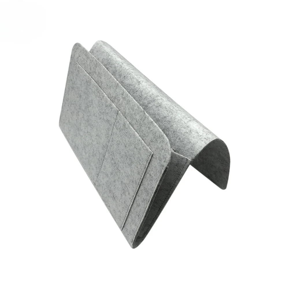 A folded grey felt bedside storage organizer with a hanging pocket.